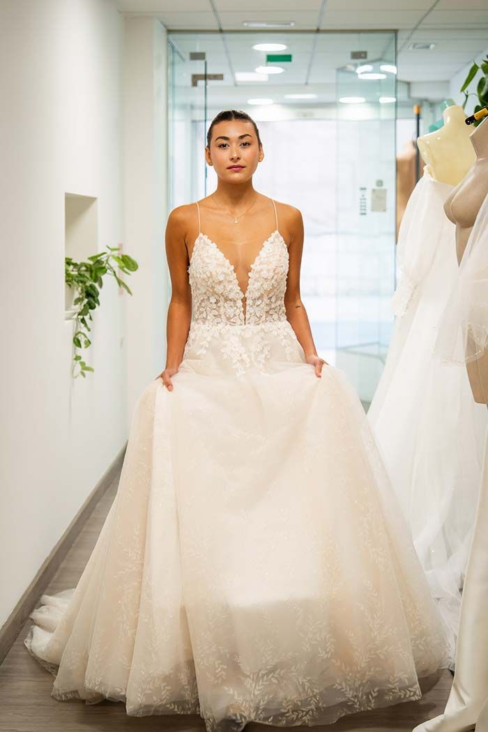 Mujer con vestido de novia sosteniendo falda, de pie en un pasillo cerca de maniquíes.