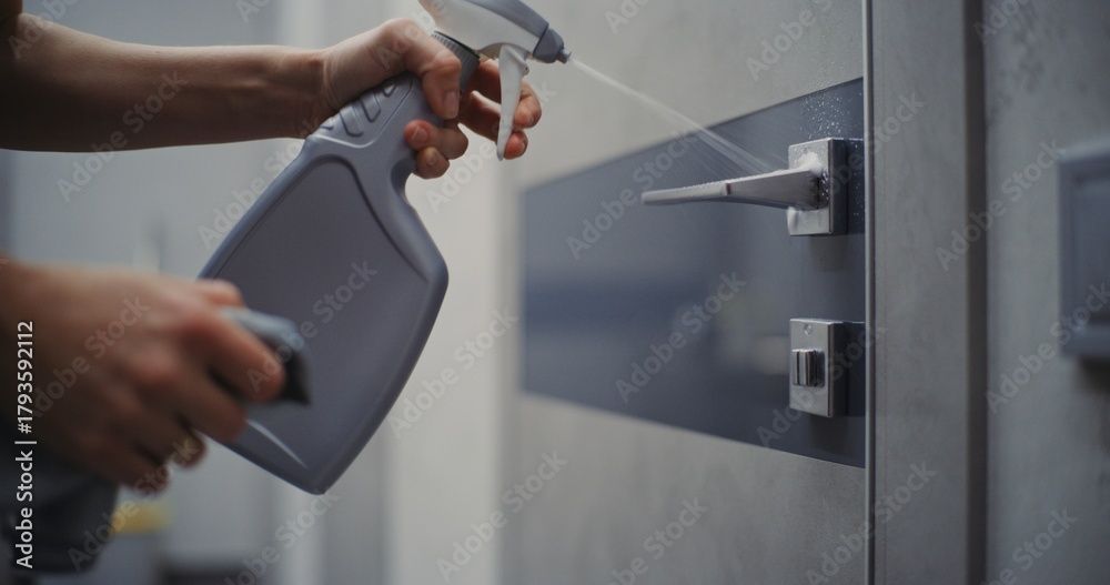 Eine Person besprüht einen Türgriff und ein Türschloss mit Desinfektionsmittel.