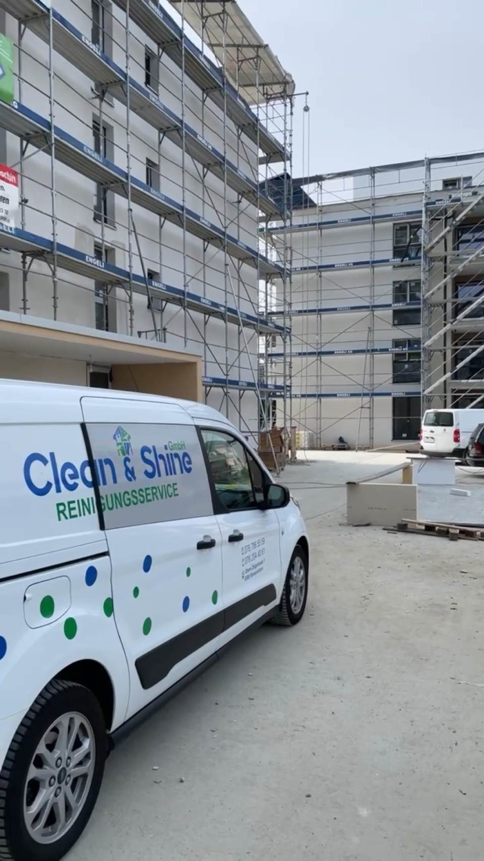 Ein weisser Lieferwagen mit dem Logo „Clean & Shine“ parkt auf einer Baustelle mit Baugerüsten an den Gebäuden.