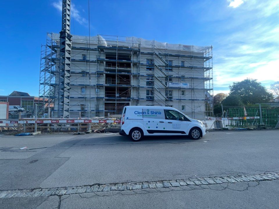 Ein weisser Lieferwagen parkt vor einem im Bau befindlichen Gebäude, das von einem Gerüst umgeben ist.