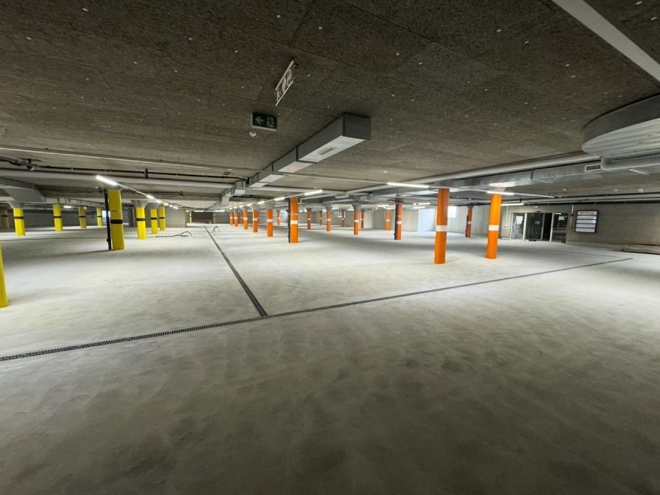 Leere Parkgarage mit Betonboden, orange und gelben Stützpfeilern und Deckenbeleuchtung.