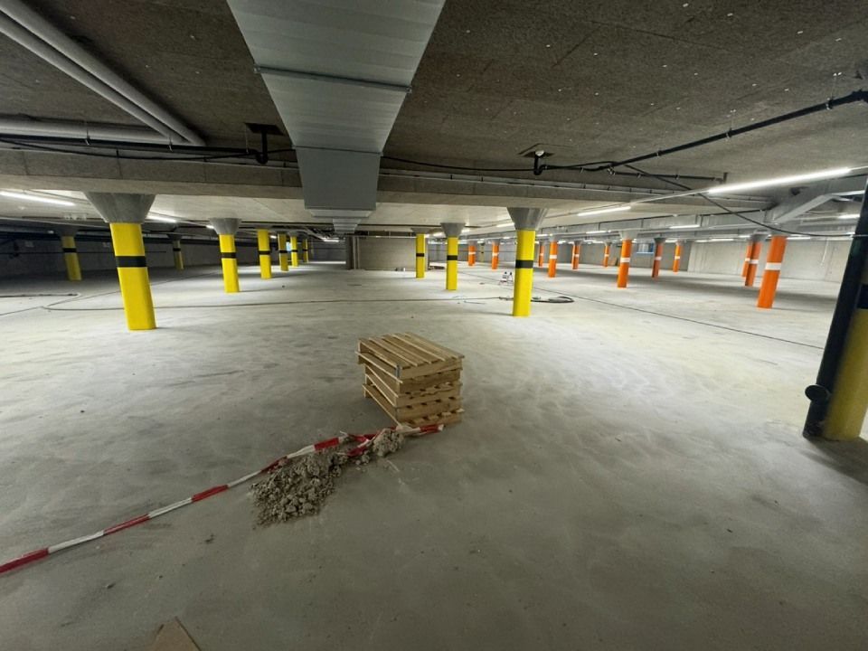 Parkhaus aus Beton mit gelben und orangen Säulen, darüber verlaufenden Rohren und einem Stapel Paletten.