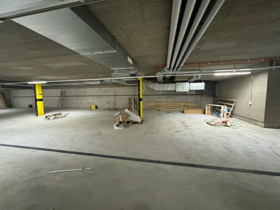 Tiefgarage mit Betonboden und unfertiger Decke, verschiedene Baumaterialien verstreut.
