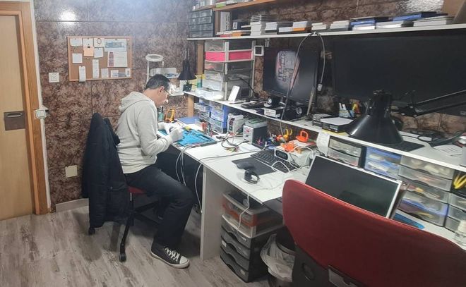 Un hombre está sentado en un escritorio en una habitación desordenada trabajando en una computadora.