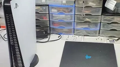 Hay una PlayStation 5 encima de un escritorio al lado de una computadora portátil.