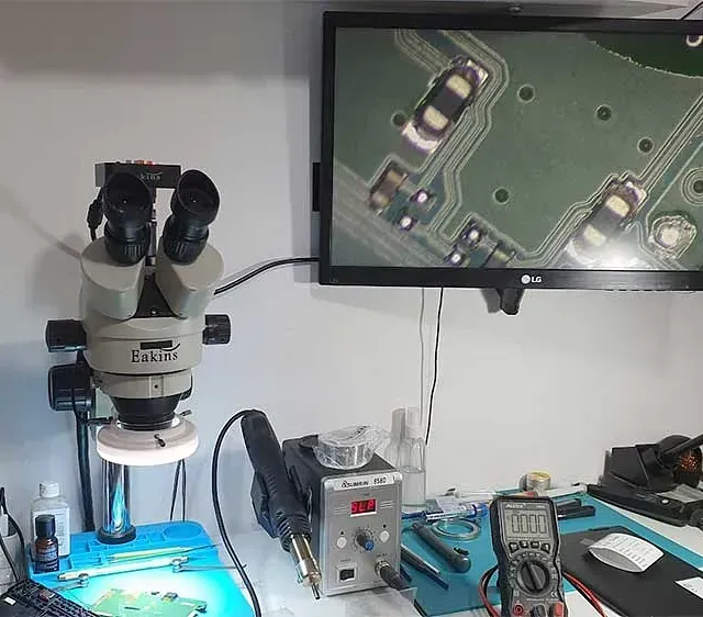 Un microscopio está sobre una mesa junto a un monitor LG.