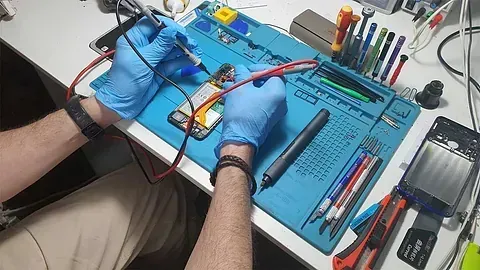 Un hombre que lleva guantes azules está trabajando en un teléfono celular.