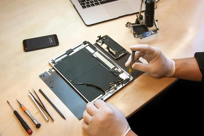 Una persona está trabajando en una tableta con una computadora portátil en el fondo.