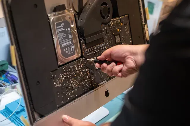 Una persona está arreglando una computadora Apple con un destornillador.