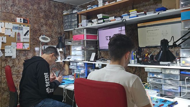 Un hombre está sentado en un escritorio en una habitación desordenada trabajando en una computadora.