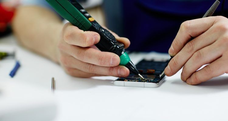 Una persona está reparando un teléfono celular con una herramienta.