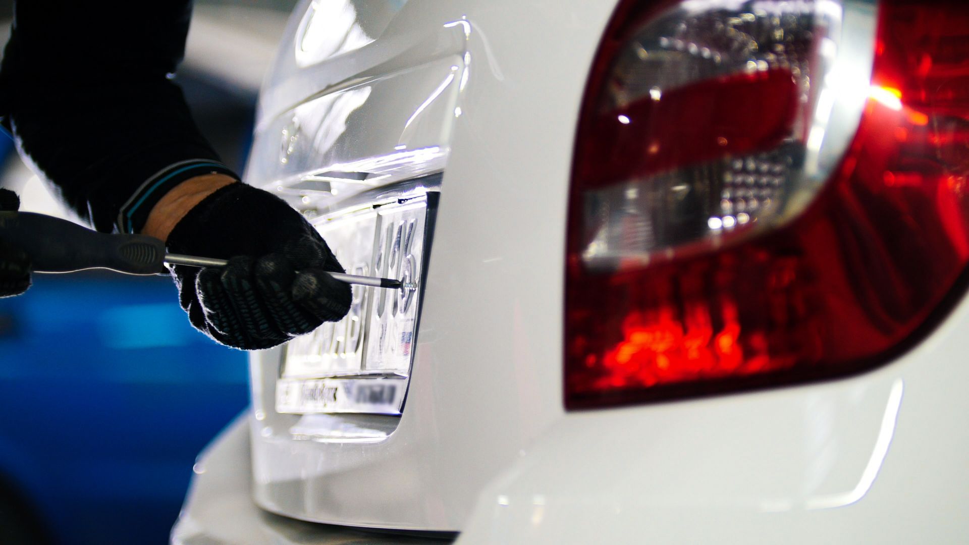 Des mains gantées fixent une plaque d'immatriculation à l'arrière d'une voiture blanche la nuit