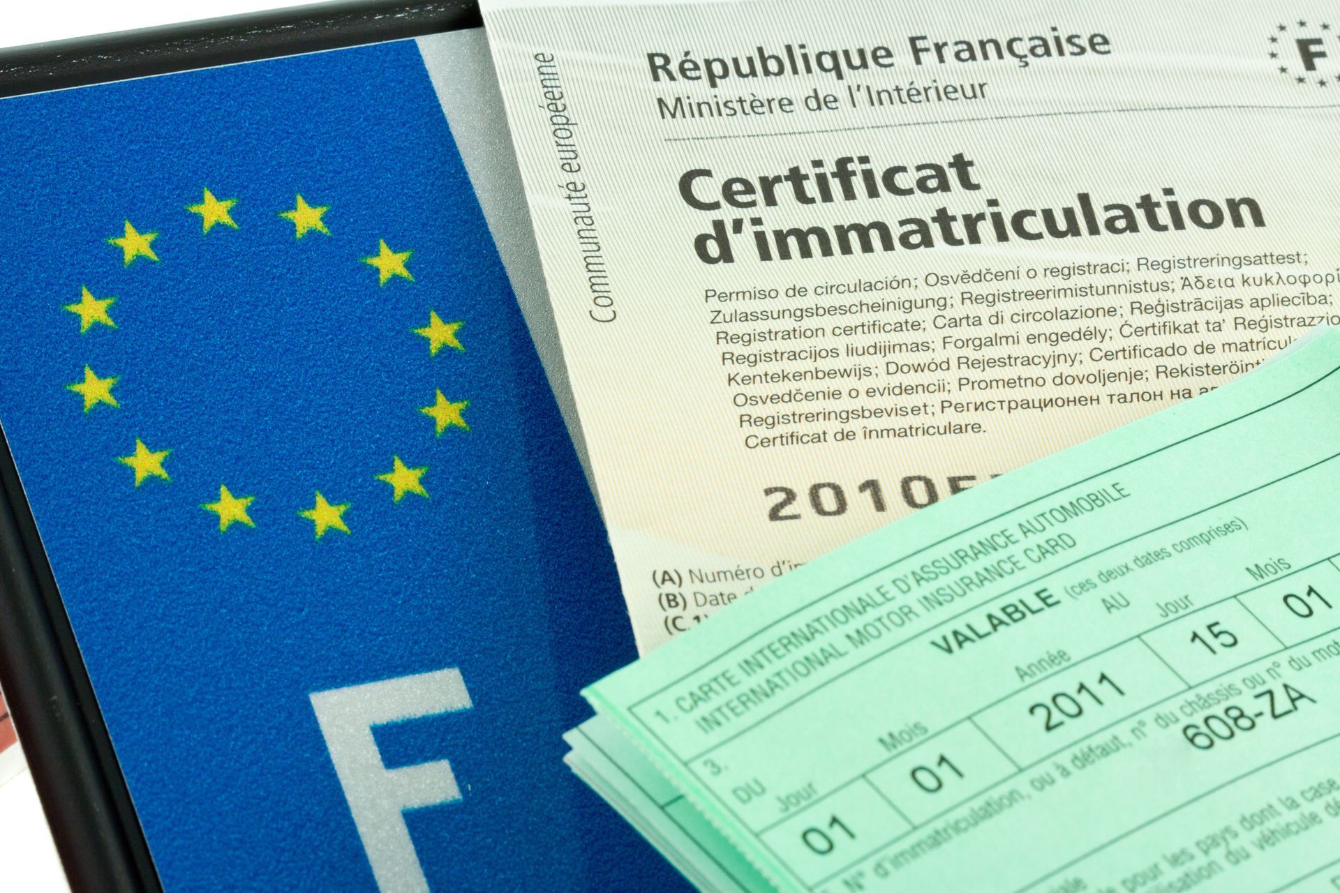 Des papiers d'immatriculation français à côté d'une plaque d'immatriculation bleue européenne avec un emoji F blanc