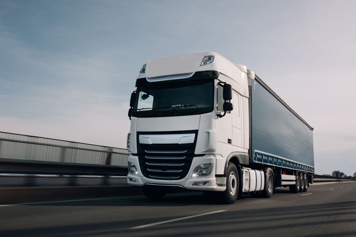 Un semi-remorque blanc circule sur une autoroute sous un ciel dégagé.