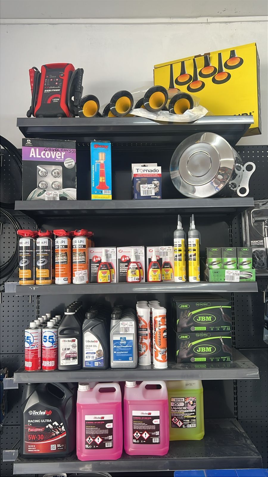Présentoir de produits d'entretien automobile sur des étagères noires, avec une sacoche à outils rouge et noire et des flacons pulvérisateurs jaunes posés dessus.