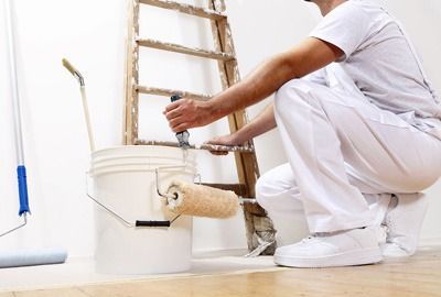 Un hombre se arrodilla mientras pinta una pared con un rodillo de pintura.