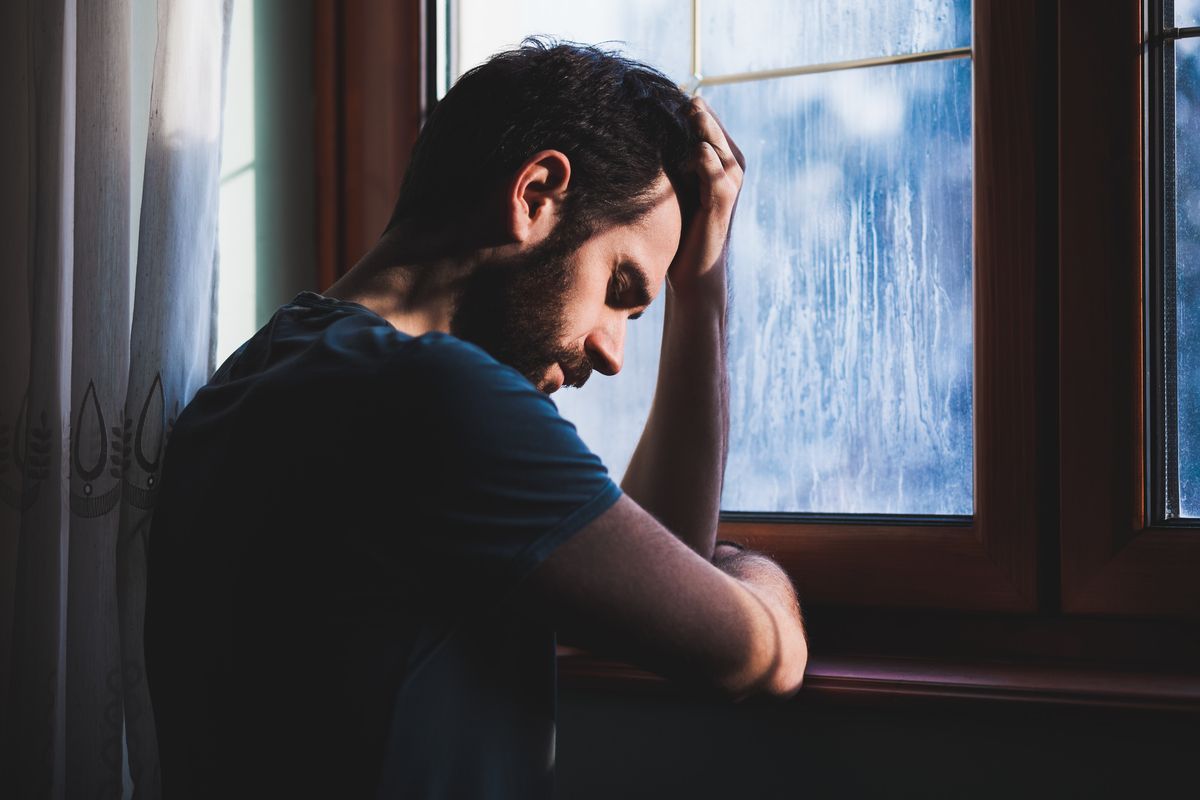 Una persona apoyada en el alféizar de una ventana, mirando hacia abajo a través de una ventana empañada por la lluvia