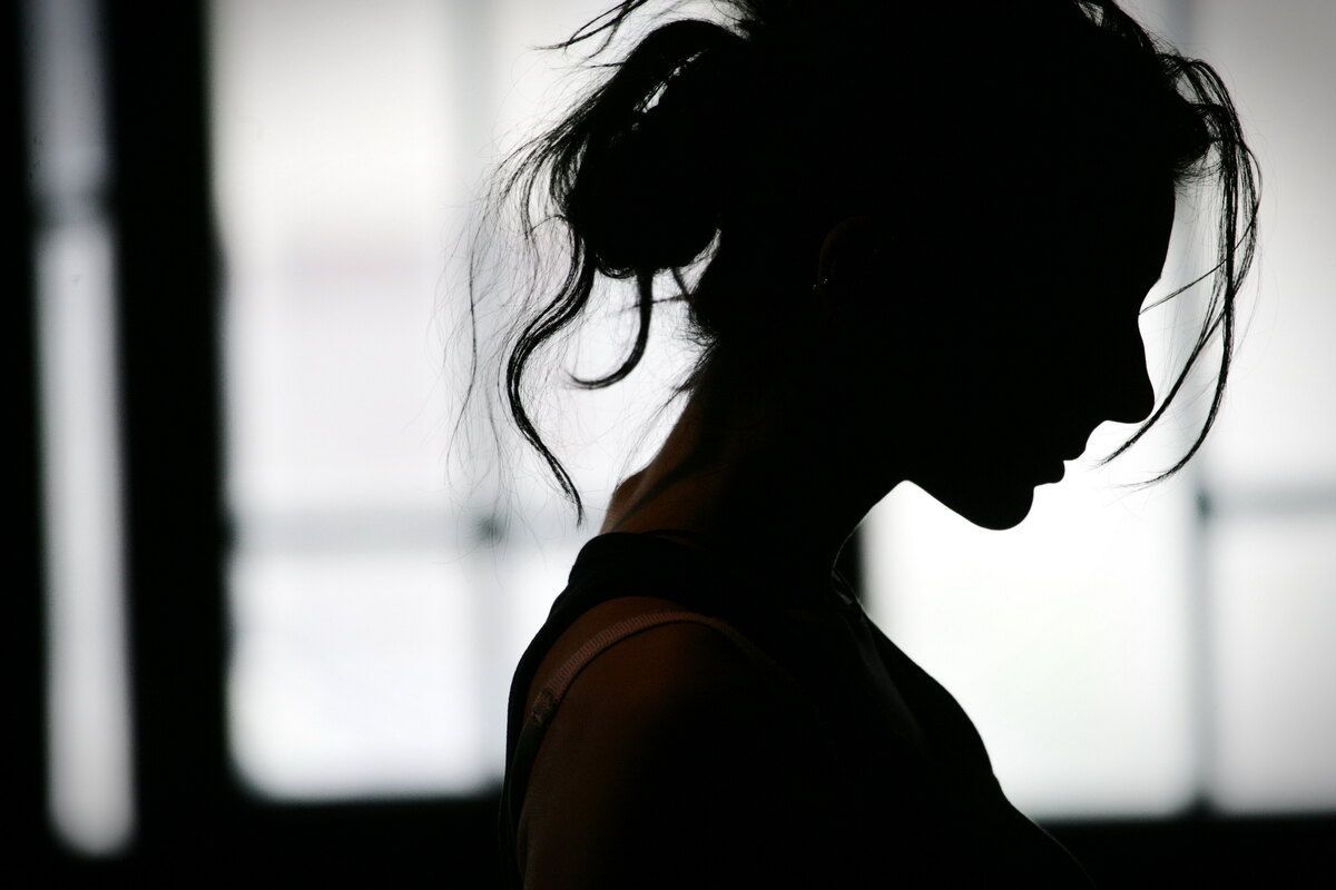 Silueta de una persona de perfil contra una ventana luminosa, con el pelo recogido.