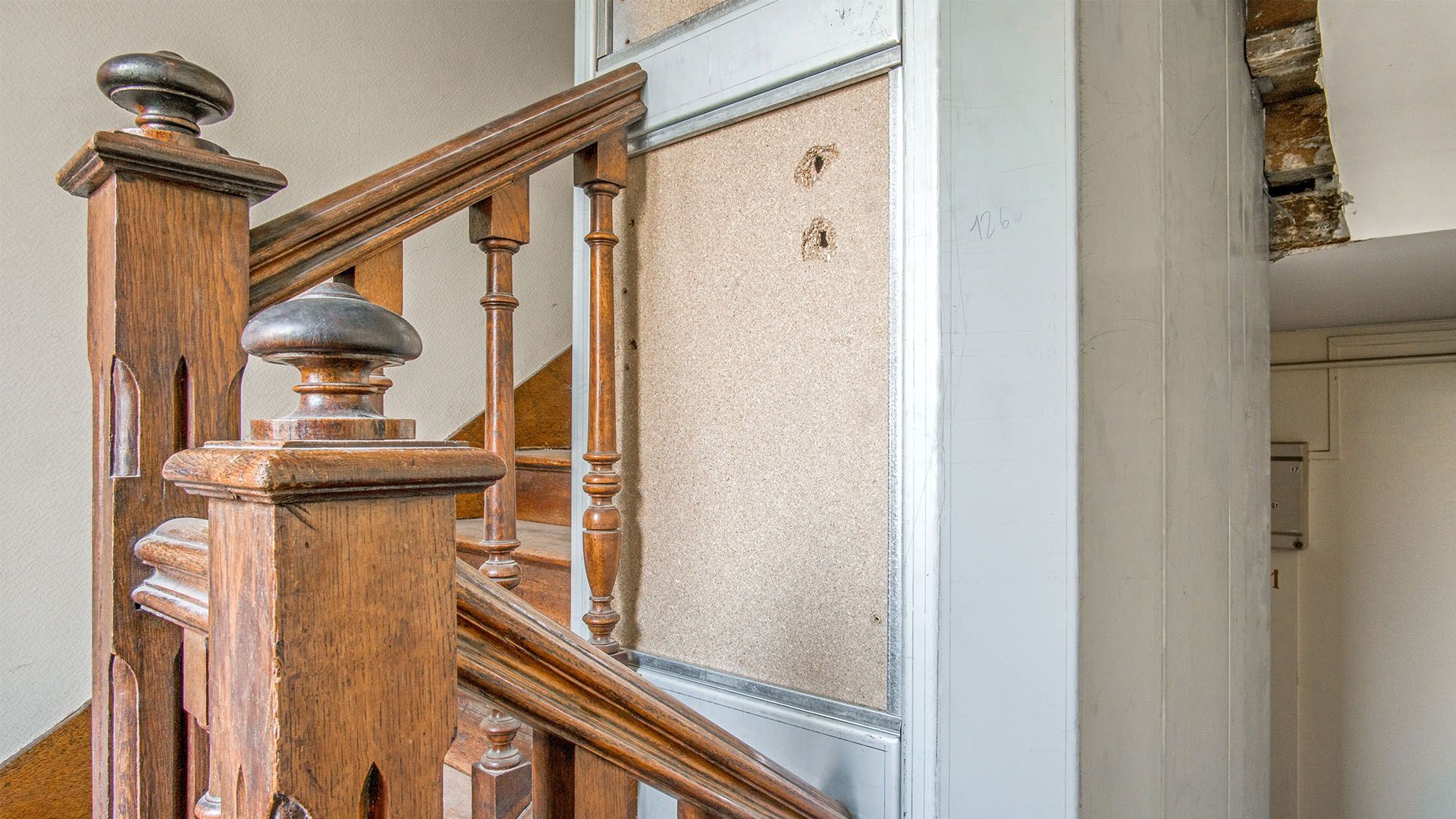 Escalier en bois avec rampe ornée et lambris texturé.
