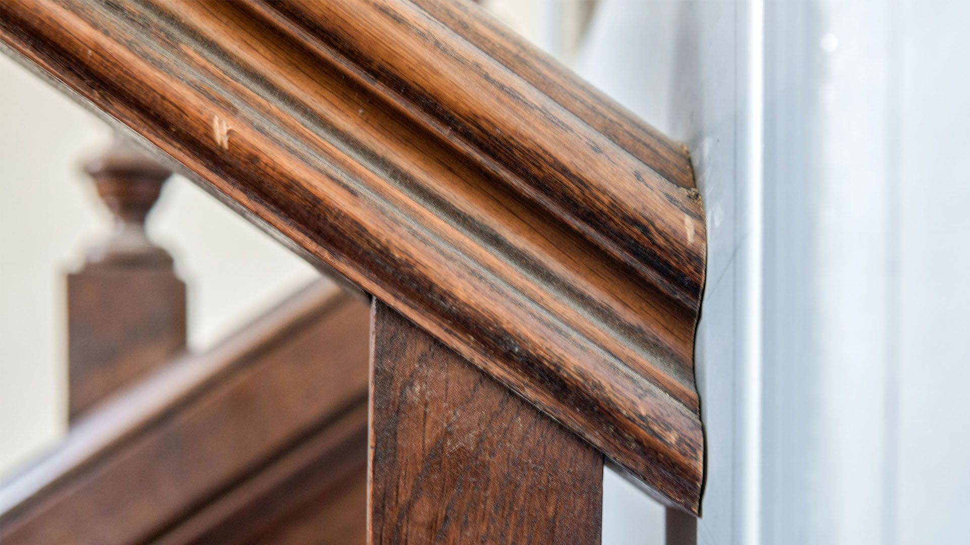 Détail d'une rampe d'escalier en bois, marron avec moulure décorative, à côté d'un mur blanc.