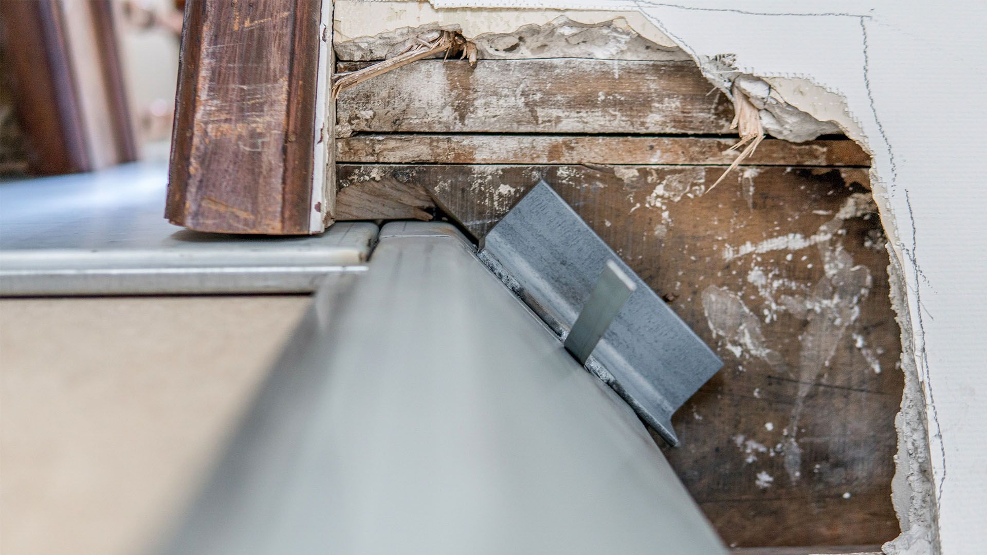 Gros plan sur l'installation des moulures de porte et des supports métalliques, avec un mur et un sol endommagés.