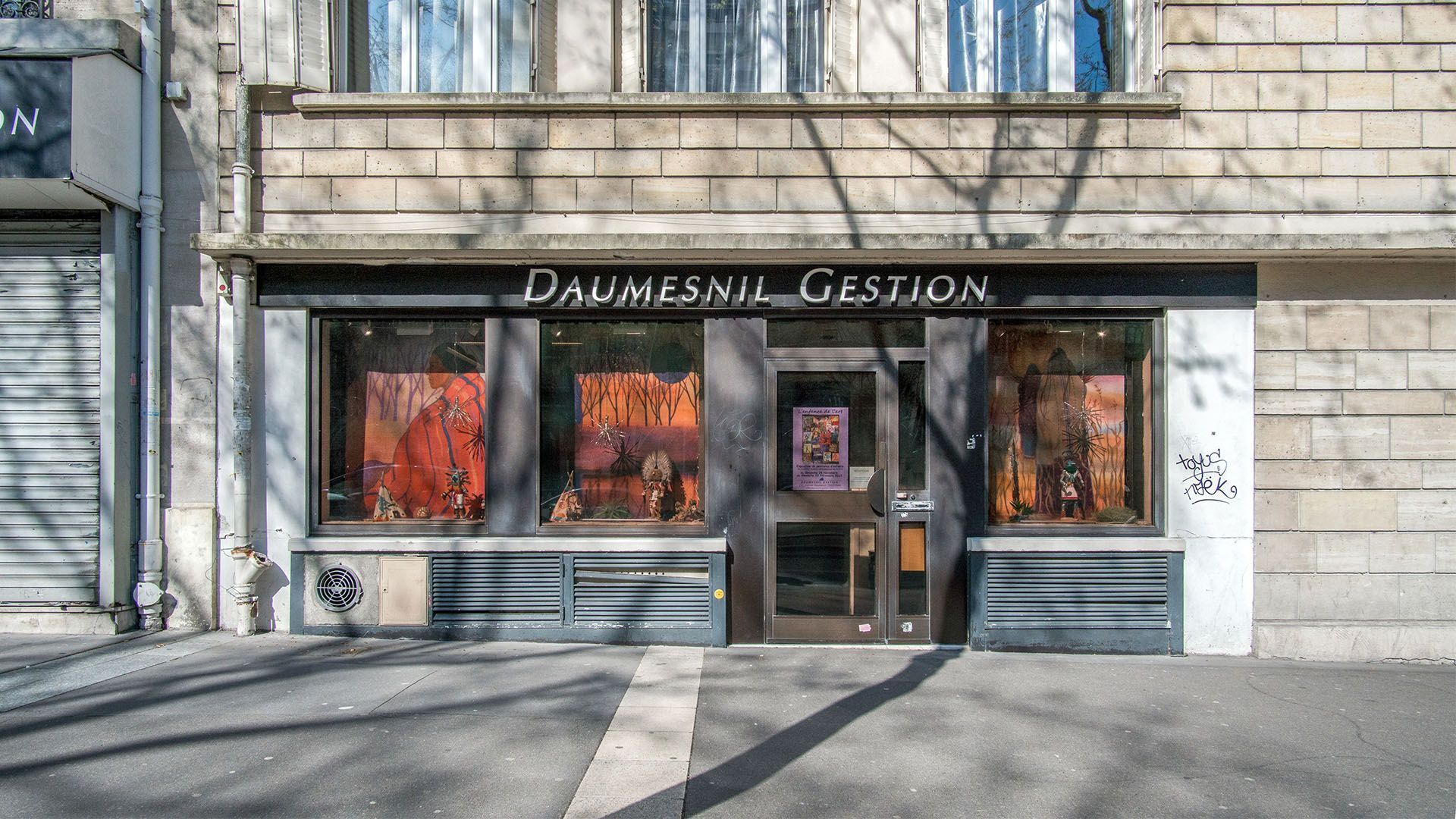 Extérieur de la façade du magasin « Daumesnil Gestion » avec vitrines et entrée centrale.