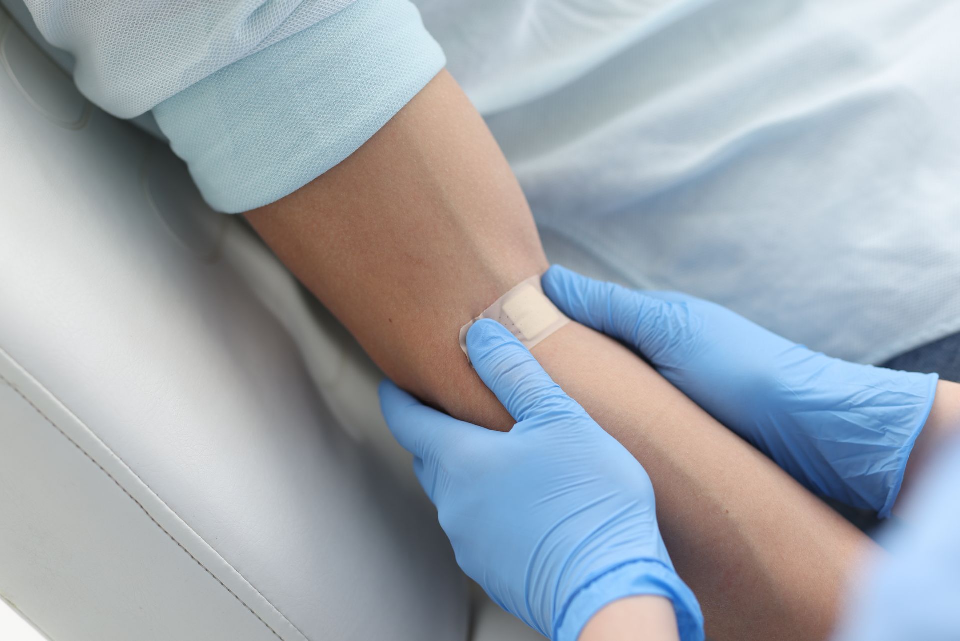 Des mains gantées appliquent un bandage sur l'avant-bras d'une personne allongée sur un lit médicalisé.