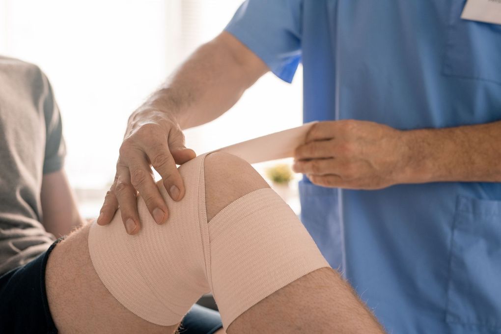Un professionnel de la santé ajuste un bandage sur le genou d'un patient dans un environnement clinique.
