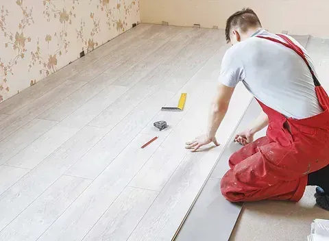 Un hombre con un mono rojo está instalando un piso de madera.