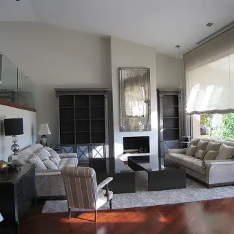 Sala de estar con techos altos, chimenea, sofás, estanterías y un gran espejo.