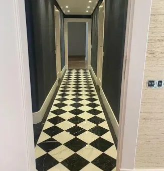 Pasillo estrecho con suelo con diseño de diamantes en blanco y negro, paredes de color azul oscuro y una puerta al final.