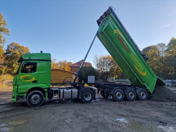 Grüner Sattelschlepper kippt Kies ab. Draußen, strahlend blauer Himmel. „Lehmann“-Branding.