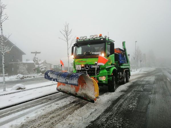 Schneepflug räumt Schnee von einer Straße in einer nebligen, verschneiten Umgebung.