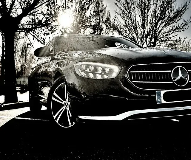 Un sedán Mercedes negro estacionado afuera; la luz del sol brilla a través de los árboles desnudos.