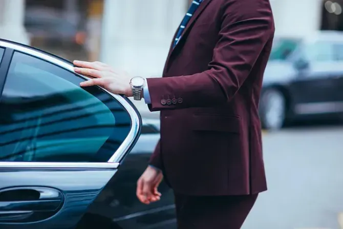 Hombre con traje marrón, con las manos en la puerta del coche, entrando.