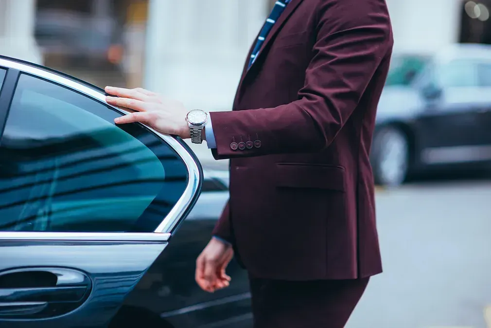 Un hombre con traje burdeos observa la puerta de un coche.