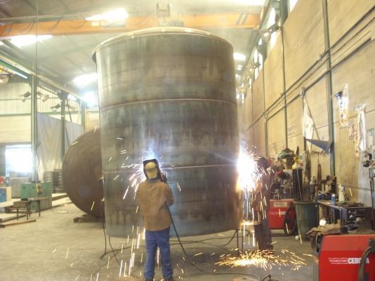 Un hombre está soldando un objeto metálico grande en una fábrica.