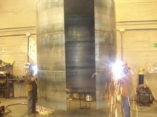 Un hombre está soldando un objeto grande de metal en una fábrica.