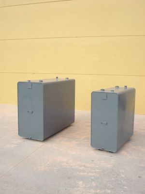 Dos cajas grises están sentadas en una acera frente a una pared amarilla.