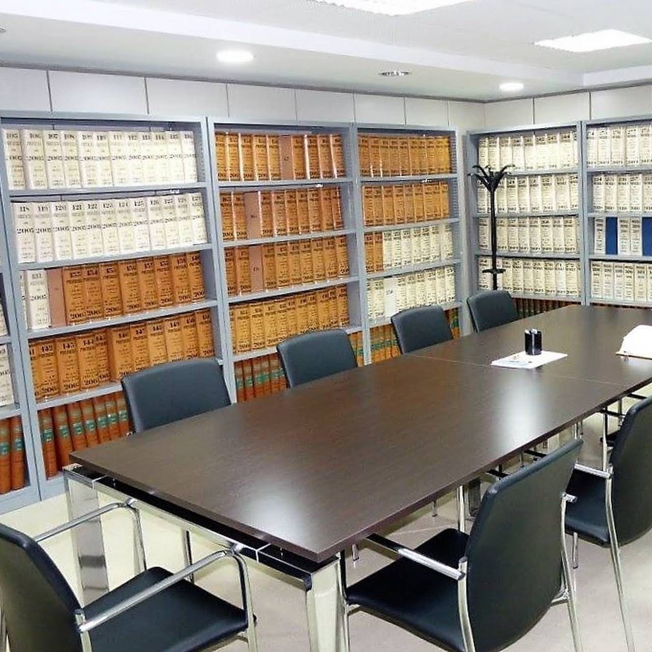 Sala de reuniones con mesa larga, sillas y estanterías llenas de archivos.