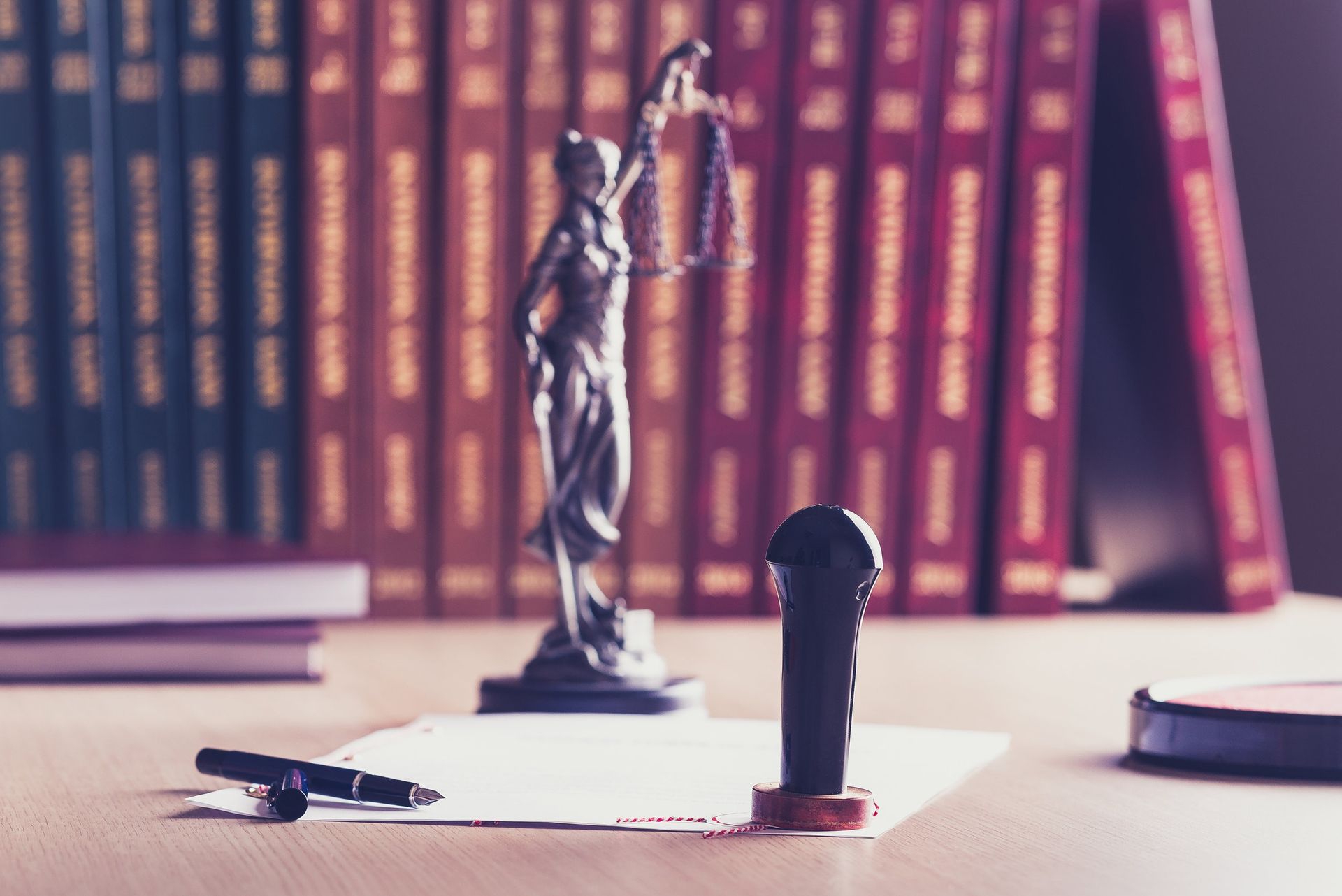 Una estatua de la Dama de la Justicia con una balanza, un sello, libros y documentos sobre un escritorio.