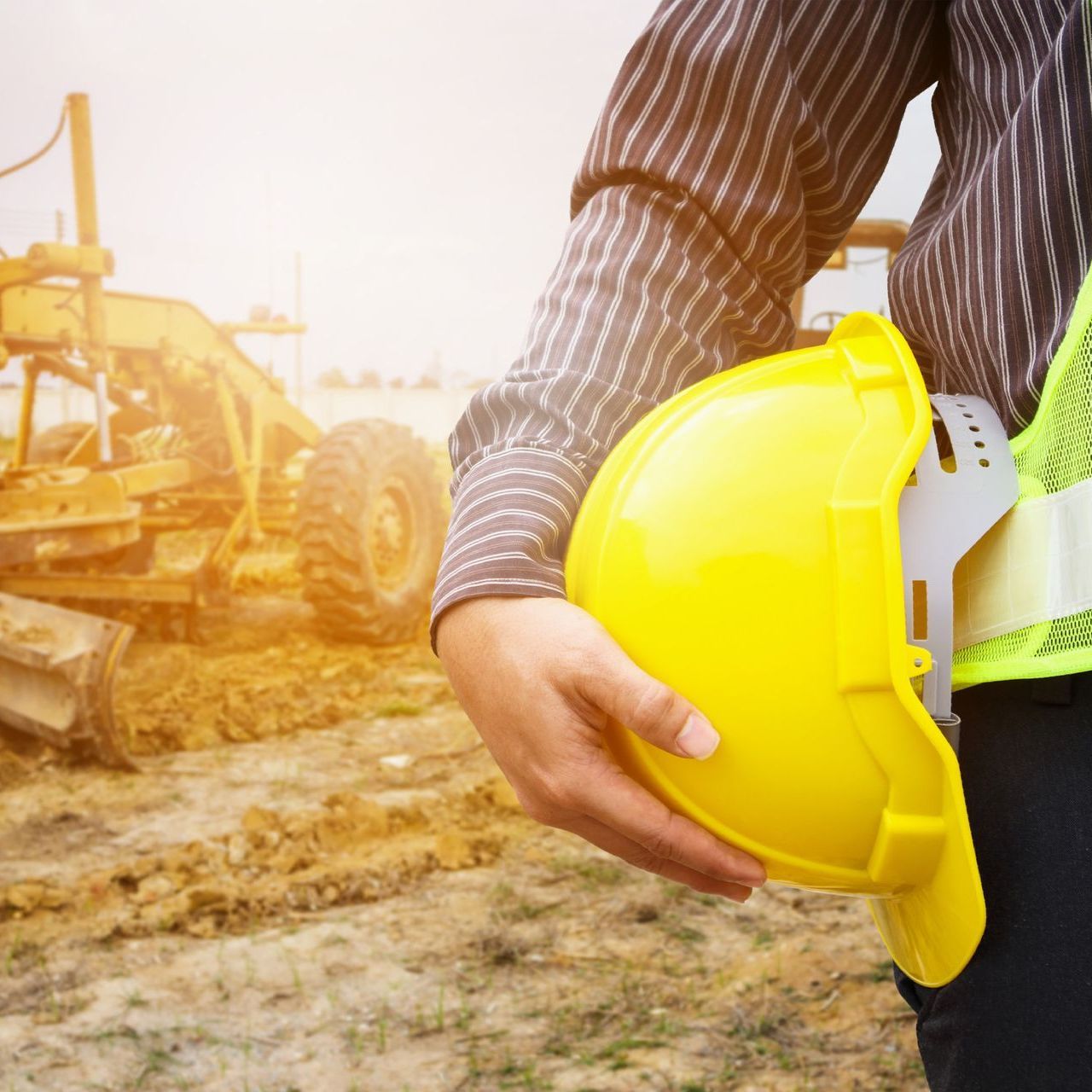 Un hombre sostiene un casco amarillo frente a un sitio de construcción.