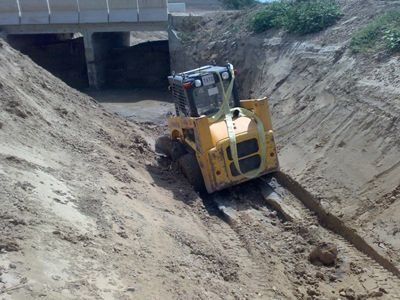 Una excavadora avanza por una colina de tierra debajo de un puente.
