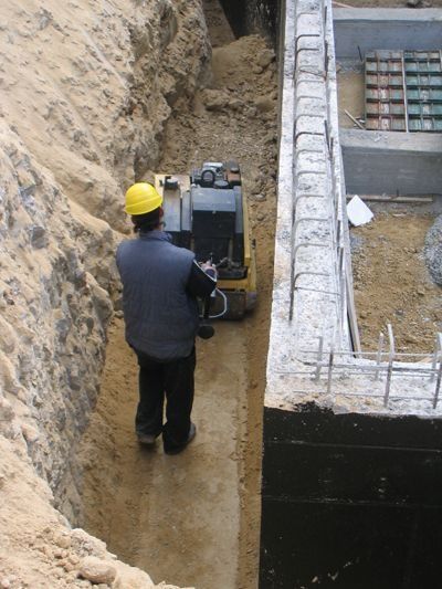 Un hombre que lleva un casco camina en una zanja junto a una excavadora.
