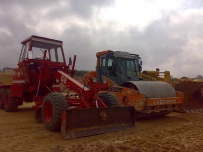 Una excavadora y un tractor están estacionados uno al lado del otro en un camino de tierra.