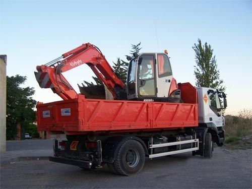 Un camión volquete rojo con una excavadora en la parte trasera