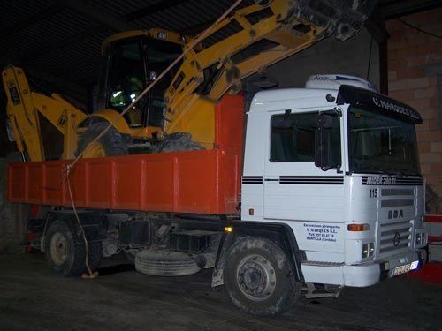 Un camión blanco con una excavadora amarilla en la parte trasera.