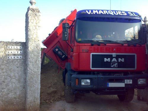 Un camión rojo está estacionado frente a un muro de piedra.