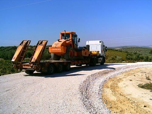 Un tractor naranja está en la parte trasera de un camión en un camino de grava.