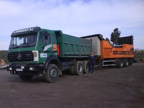 Un hombre está parado junto a un camión volquete verde.